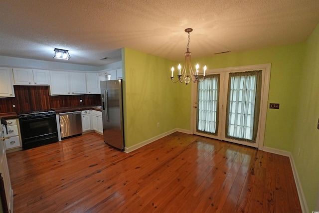 kitchen featuring stainless steel appliances, dark countertops, white cabinets, a chandelier, and baseboards