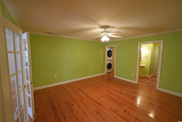 spare room with stacked washer / drying machine, crown molding, a ceiling fan, hardwood / wood-style floors, and baseboards
