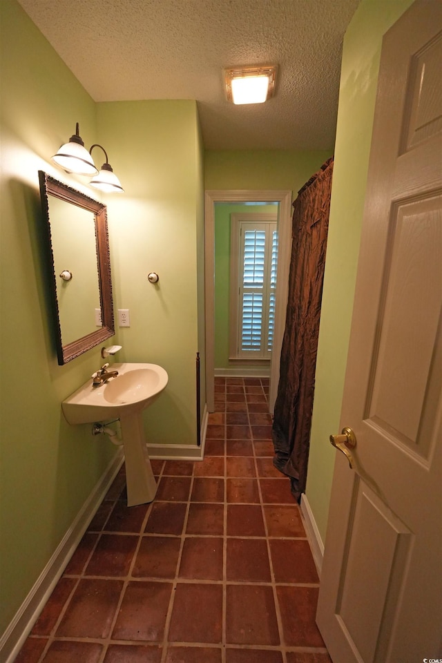 bathroom featuring a textured ceiling, a shower with shower curtain, baseboards, tile patterned floors, and a sink