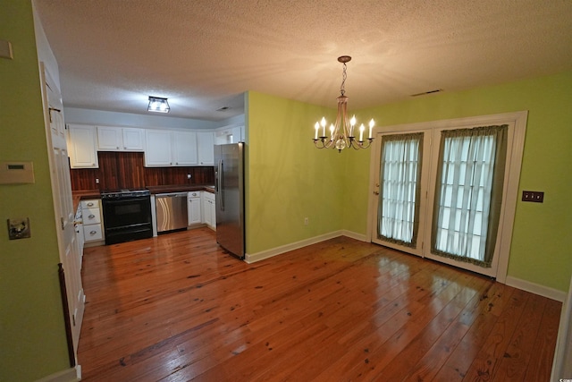 kitchen featuring appliances with stainless steel finishes, a chandelier, white cabinets, hardwood / wood-style floors, and dark countertops