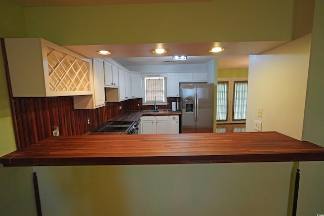 kitchen featuring stainless steel refrigerator with ice dispenser, butcher block countertops, a peninsula, healthy amount of natural light, and recessed lighting