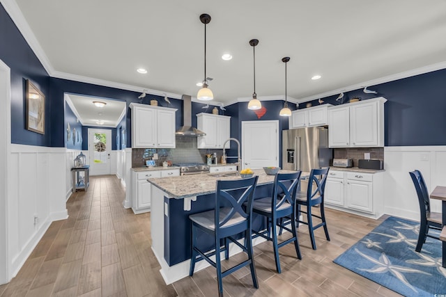 1009 Oak Marsh Ln, North Myrtle Beach, SC 29582 - kitchen with wall chimney exhaust hood, stainless steel appliances, crown molding, wainscoting, and white cabinetry