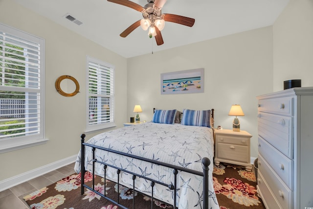 bedroom featuring multiple windows, baseboards, a ceiling fan, and wood finished floors