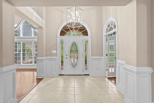 foyer entrance featuring a chandelier, plenty of natural light, a decorative wall, wainscoting, and a towering ceiling