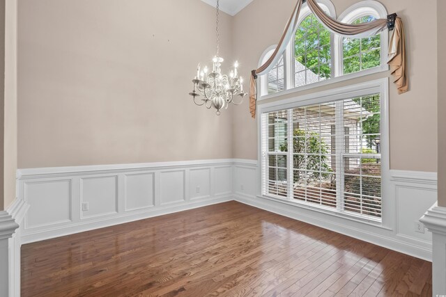 unfurnished dining area featuring a chandelier, a wainscoted wall, wood finished floors, and a decorative wall