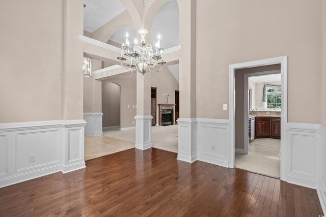 unfurnished dining area with hardwood / wood-style flooring, a chandelier, arched walkways, a wainscoted wall, and a decorative wall