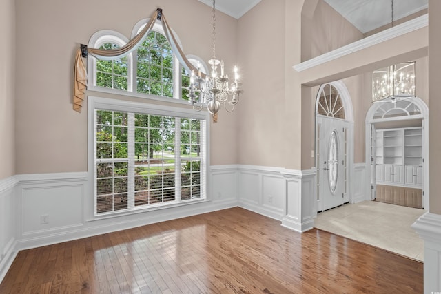 foyer entrance featuring a chandelier, wainscoting, hardwood / wood-style flooring, a towering ceiling, and a decorative wall