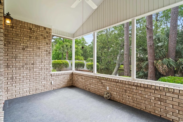 unfurnished sunroom with a ceiling fan, lofted ceiling, and view of wooded area