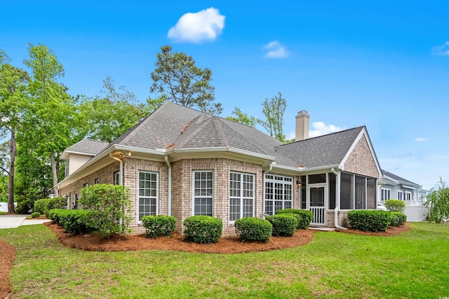 rear view of property with a sunroom, a lawn, roof with shingles, a chimney, and brick siding