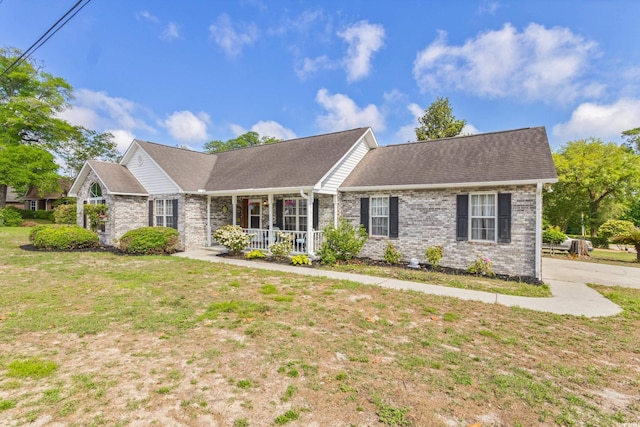 view of front of home featuring a porch, brick siding, a front lawn, and a shingled roof