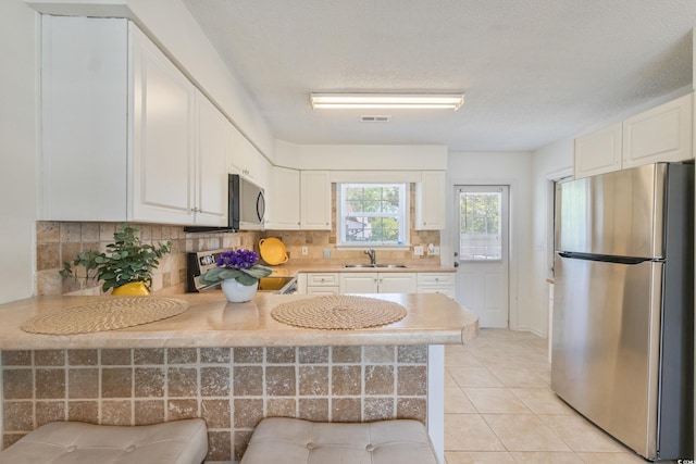kitchen featuring stainless steel appliances, a sink, decorative backsplash, a peninsula, and light countertops