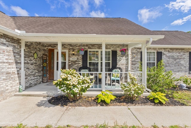entrance to property featuring a porch, brick siding, and a shingled roof