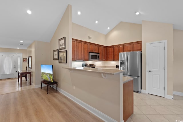 kitchen with stainless steel appliances, light countertops, a peninsula, baseboards, and a kitchen bar