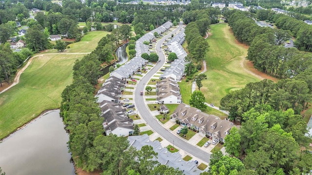 view of property location featuring a tree filled landscape, a golf course, a nearby body of water, and nearby suburban area