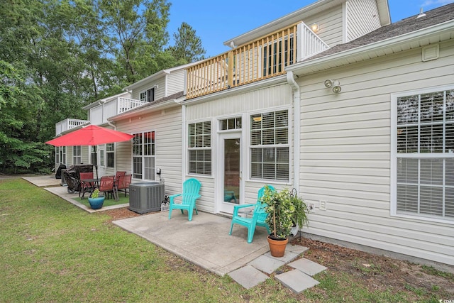 rear view of property with a balcony, a patio, central AC unit, and a yard
