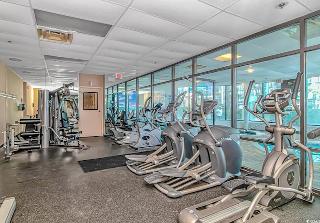 gym featuring a baseboard heating unit, a wall of windows, and a paneled ceiling