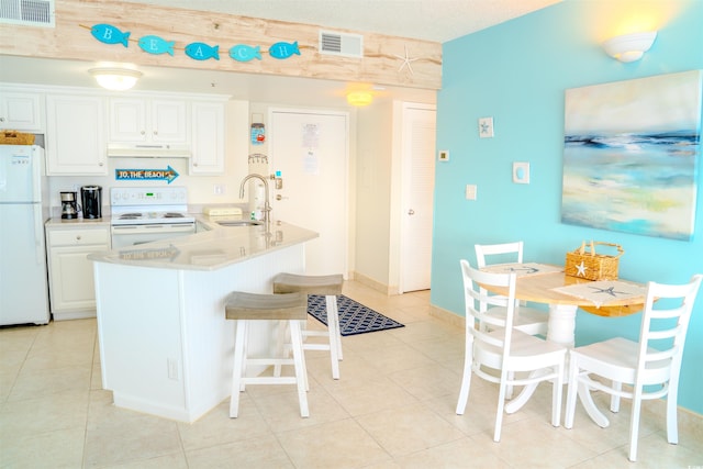 kitchen featuring white appliances, a sink, a kitchen bar, and light tile patterned floors