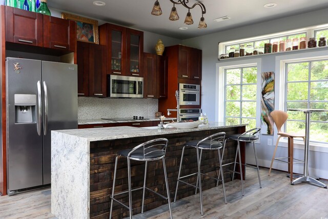 kitchen featuring stainless steel appliances, light wood-type flooring, dark brown cabinets, an island with sink, and a kitchen breakfast bar