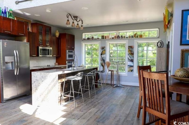 kitchen featuring appliances with stainless steel finishes, a breakfast bar area, wood finished floors, glass insert cabinets, and decorative backsplash