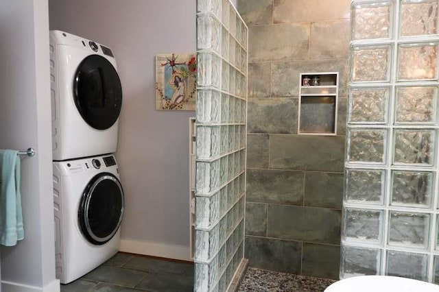 laundry area featuring stacked washer / dryer, baseboards, and tile patterned flooring