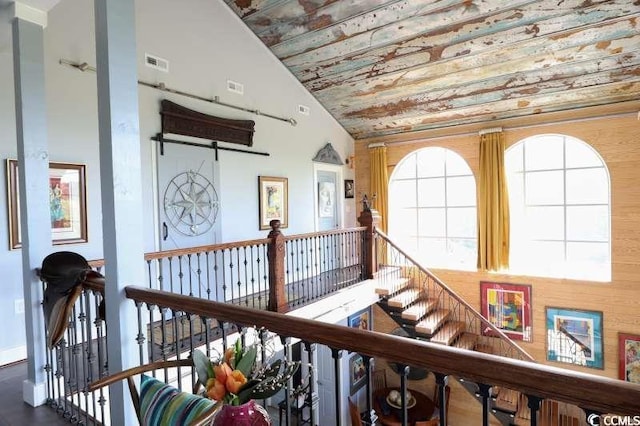hallway with an upstairs landing, high vaulted ceiling, and wooden ceiling