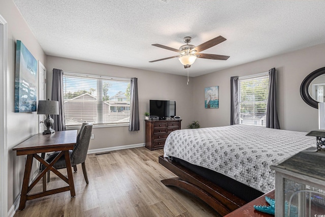bedroom with light wood-style flooring, a textured ceiling, baseboards, and a ceiling fan