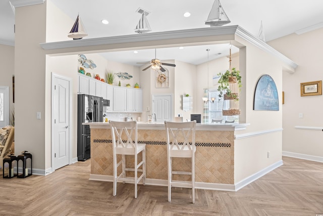 kitchen with black refrigerator with ice dispenser, baseboards, a kitchen bar, ceiling fan, and light countertops