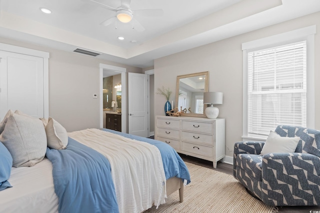 bedroom with wood finished floors, recessed lighting, connected bathroom, baseboards, and a raised ceiling