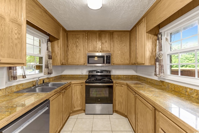 kitchen featuring appliances with stainless steel finishes, a sink, a textured ceiling, light tile patterned floors, and brown cabinetry