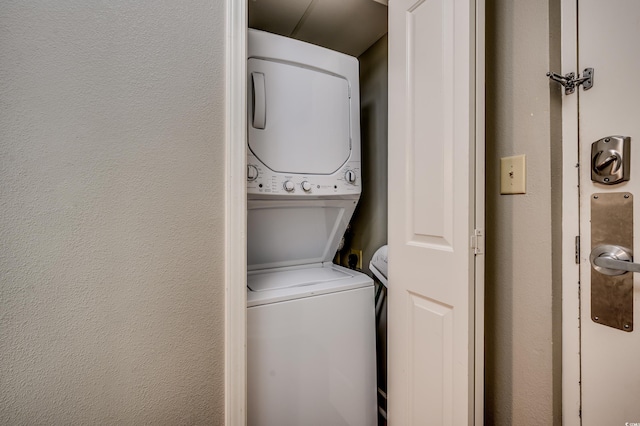 clothes washing area featuring stacked washer and clothes dryer and a textured wall