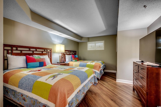 bedroom with baseboards, wood finished floors, and a textured ceiling