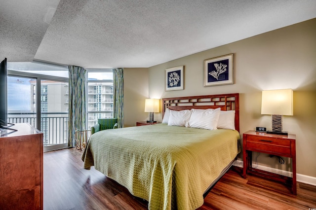 bedroom with access to outside, a textured ceiling, wood finished floors, expansive windows, and baseboards