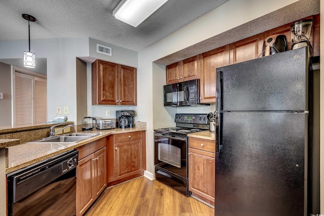 kitchen featuring black appliances, a sink, light wood-style floors, brown cabinetry, and a textured ceiling