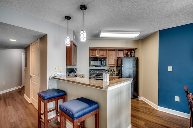 kitchen featuring black appliances, a textured ceiling, baseboards, dark wood-style floors, and a kitchen breakfast bar