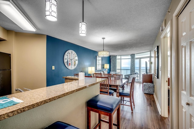 kitchen featuring wood finished floors, a textured ceiling, hanging light fixtures, freestanding refrigerator, and open floor plan