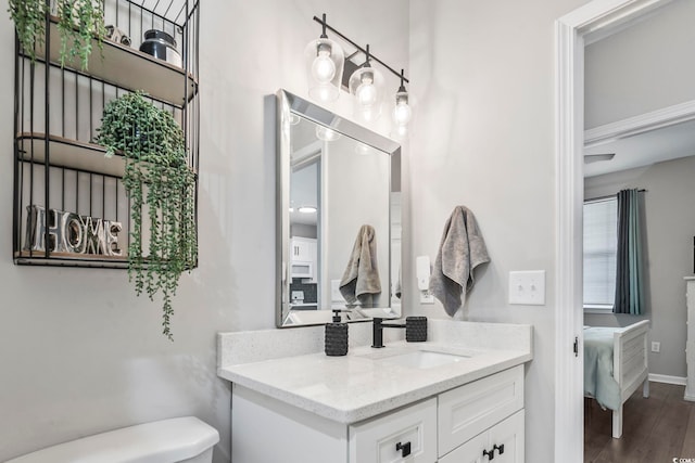 ensuite bathroom with vanity, toilet, wood finished floors, and baseboards