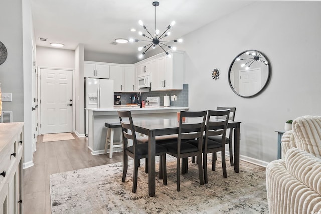 dining space with a chandelier, light wood-style flooring, and baseboards