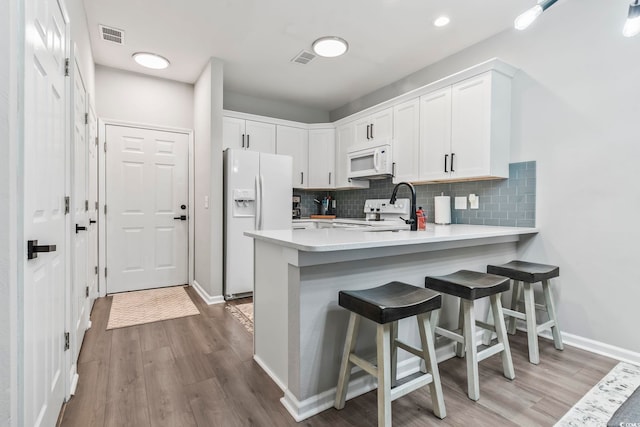 kitchen featuring white appliances, a peninsula, a sink, white cabinetry, and decorative backsplash