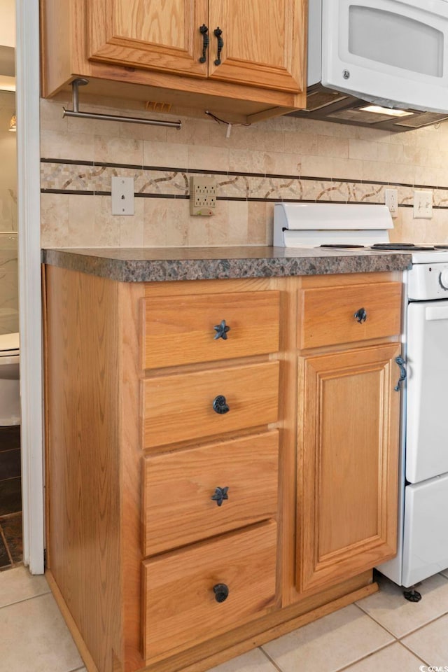 kitchen featuring white appliances, light tile patterned floors, dark countertops, and tasteful backsplash