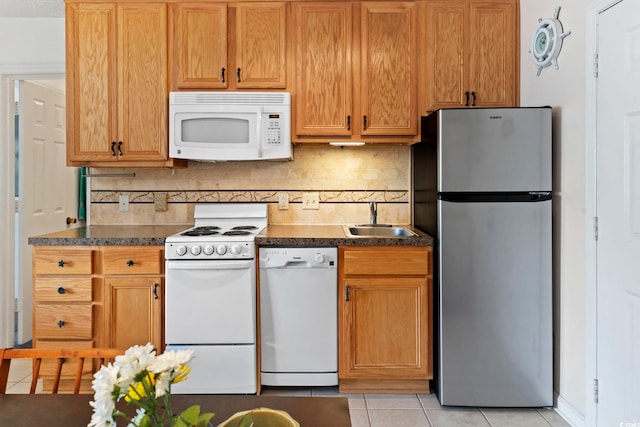 kitchen featuring white appliances, a sink, light tile patterned floors, dark countertops, and decorative backsplash