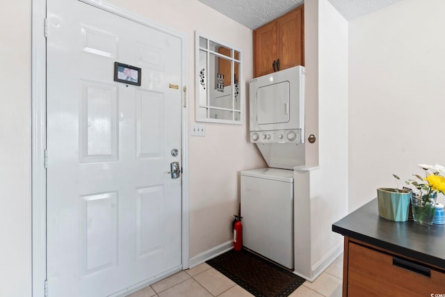 washroom featuring stacked washing machine and dryer, light tile patterned flooring, a textured ceiling, baseboards, and cabinet space