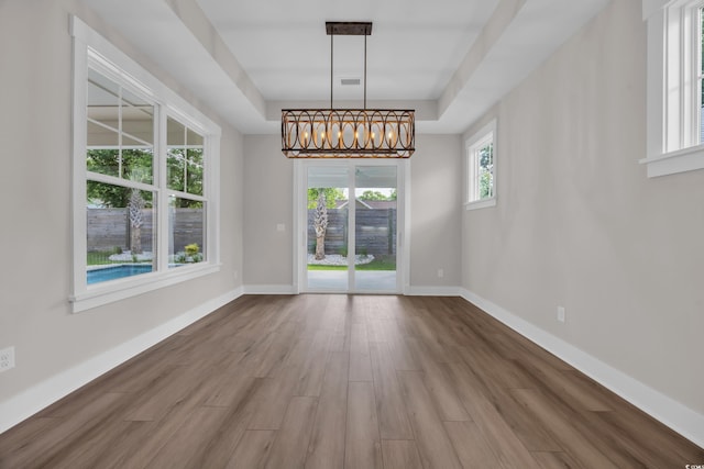 unfurnished dining area featuring wood finished floors, a chandelier, baseboards, and a tray ceiling