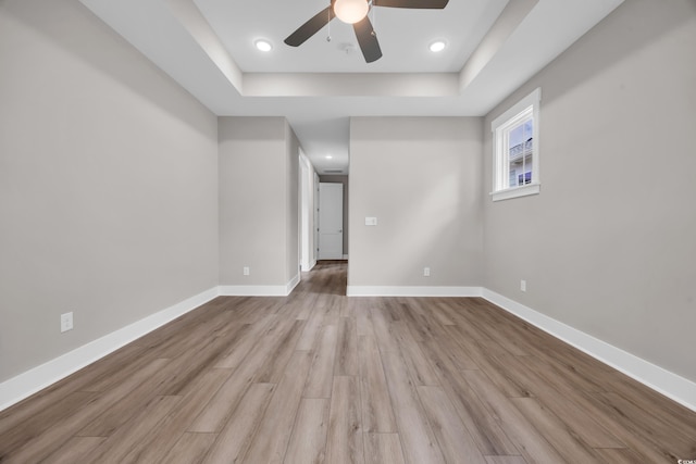 unfurnished room with a ceiling fan, a tray ceiling, light wood-type flooring, baseboards, and recessed lighting