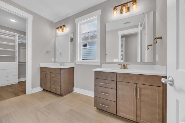 full bathroom featuring two vanities, a spacious closet, and baseboards