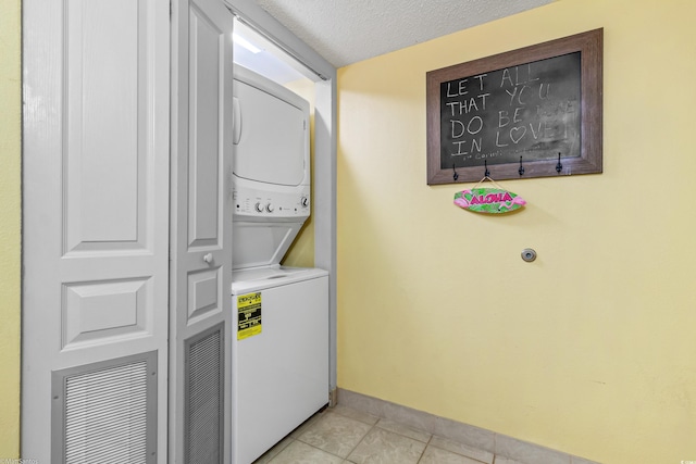 clothes washing area featuring stacked washer and clothes dryer, light tile patterned floors, baseboards, and a textured ceiling