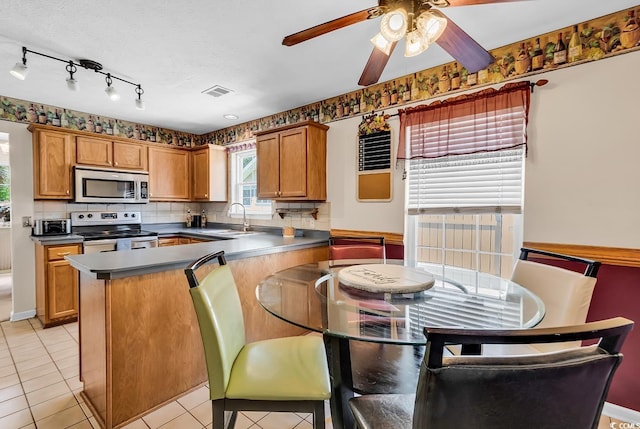 kitchen with stainless steel appliances, a sink, brown cabinets, a peninsula, and dark countertops