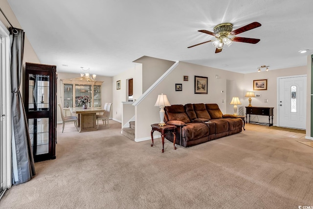 living area with light colored carpet, stairs, a ceiling fan, a chandelier, and baseboards