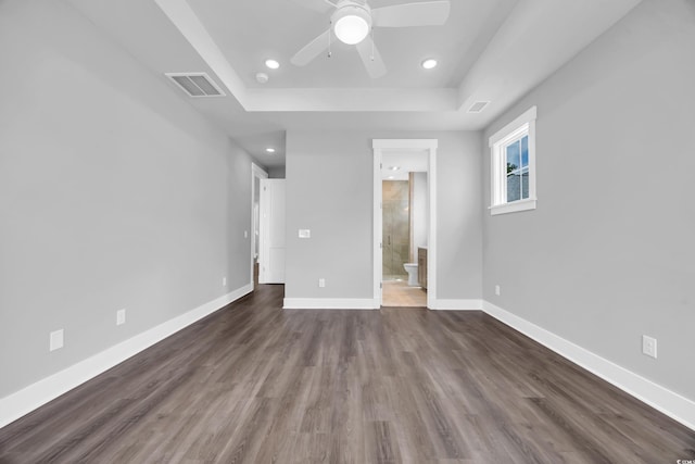 unfurnished bedroom featuring a raised ceiling, recessed lighting, dark wood-style floors, baseboards, and ensuite bath