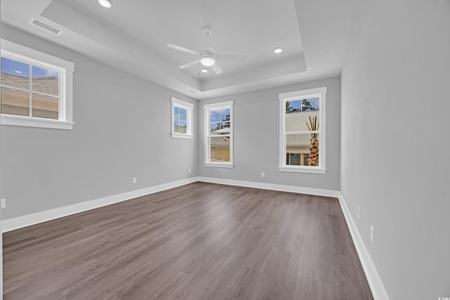empty room featuring a tray ceiling, healthy amount of natural light, dark wood-type flooring, baseboards, and recessed lighting