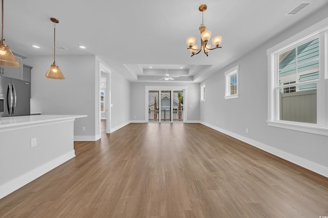unfurnished living room with recessed lighting, wood finished floors, a chandelier, a raised ceiling, and baseboards